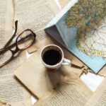 A flat lay of vintage papers, a coffee cup, a folded map, and eyeglasses creates a nostalgic travel theme.