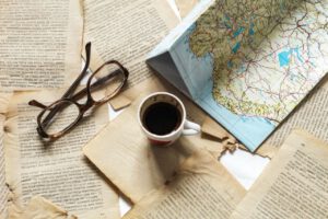 A flat lay of vintage papers, a coffee cup, a folded map, and eyeglasses creates a nostalgic travel theme.