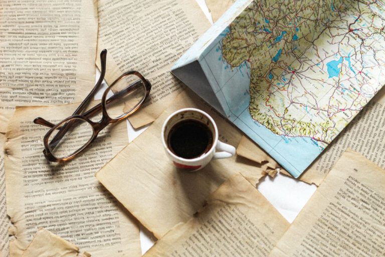 A flat lay of vintage papers, a coffee cup, a folded map, and eyeglasses creates a nostalgic travel theme.