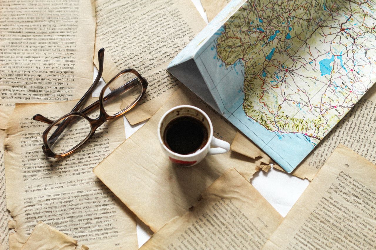 A flat lay of vintage papers, a coffee cup, a folded map, and eyeglasses creates a nostalgic travel theme.